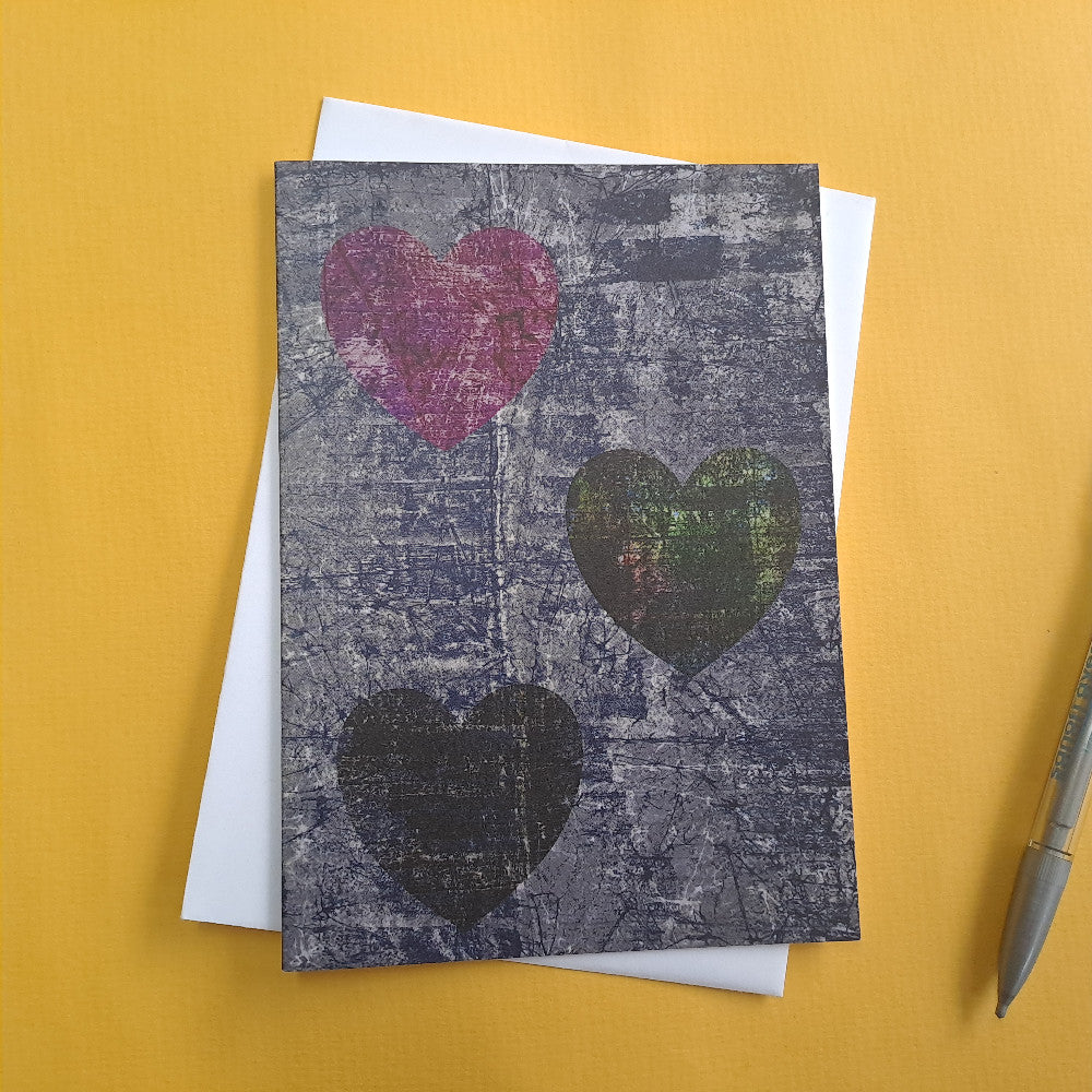 Grey greeting card featuring three love hearts over white envelope 